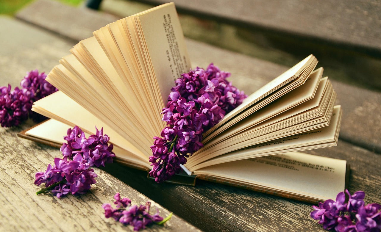 Book open on a picnic table with sprigs of lilacs